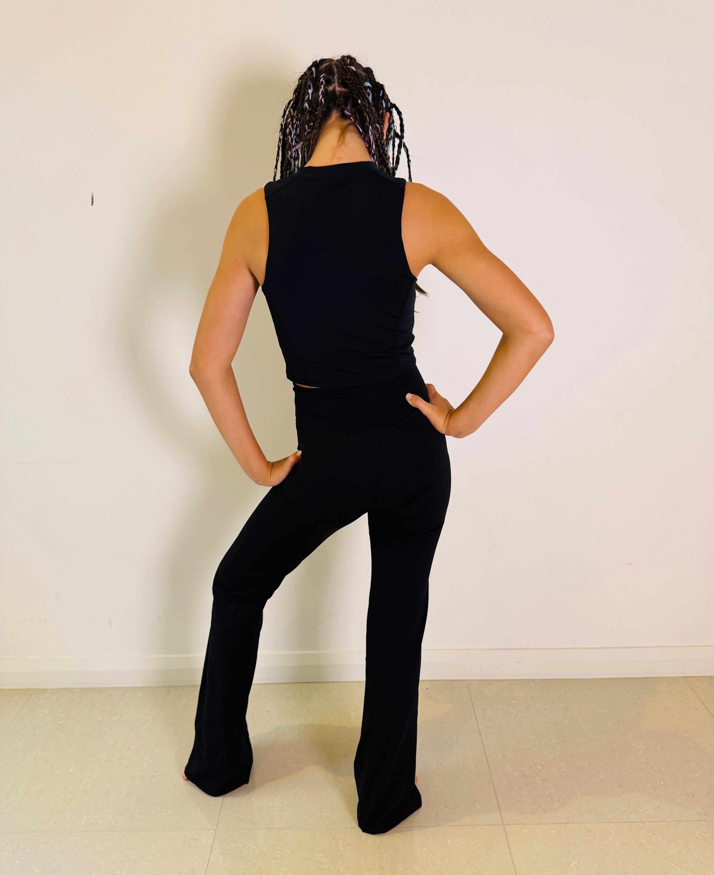 Person wearing a black sleeveless top and pants against a white wall.