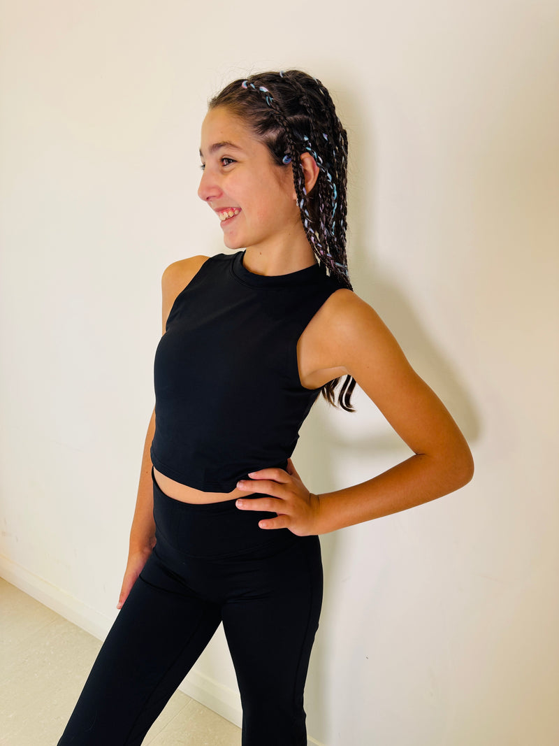 Person wearing a black sleeveless top and leggings against a white wall.